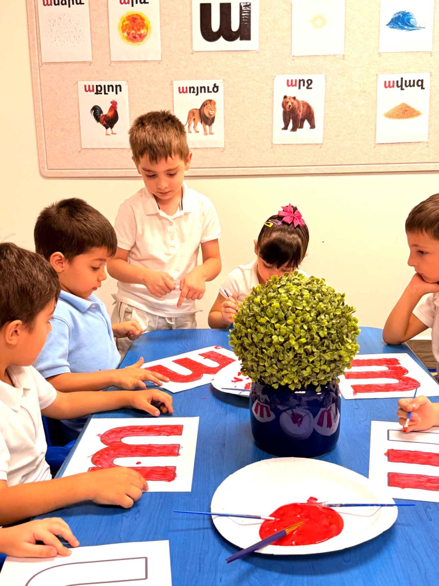 Kindergarten students practicing Armenian letters together at a classroom table